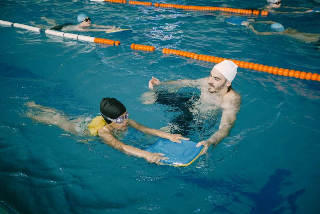 Na zdjęciu mężczyzna uczy dziecko pływać. Oboje w basenie.
